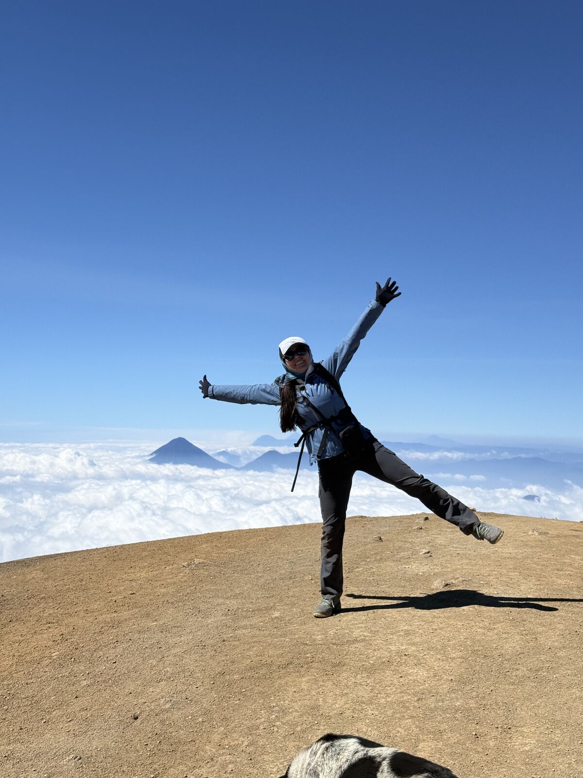 Andrea Cardona celebra con un salto en la cumbre del Acatenango, con volcanes sobre las nubes al fondo